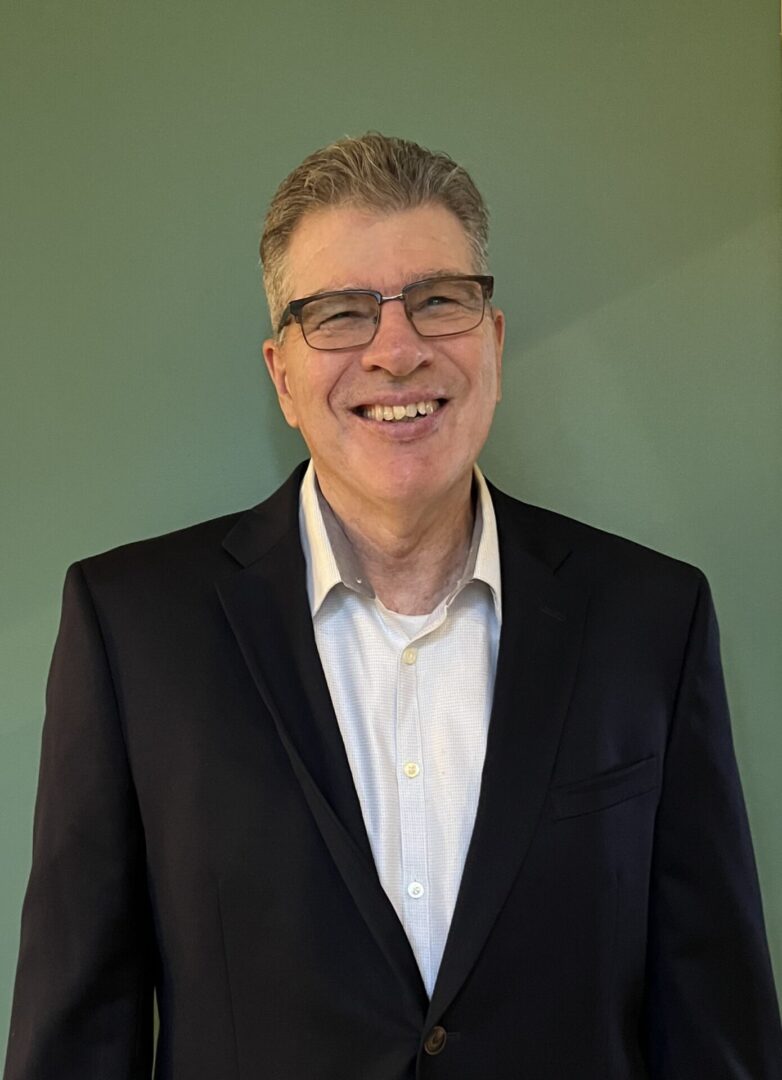 A man in a suit and glasses smiling for the camera.